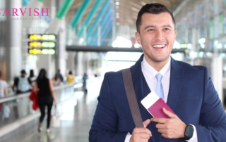 Man in suit walking through airport or train station with passport in hand and bag over shoulder. He is smiling and excited.