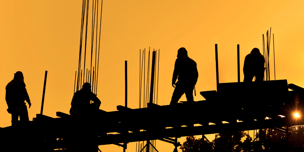 Black silhouette with an orange sky background of construction workers working up on a structure.